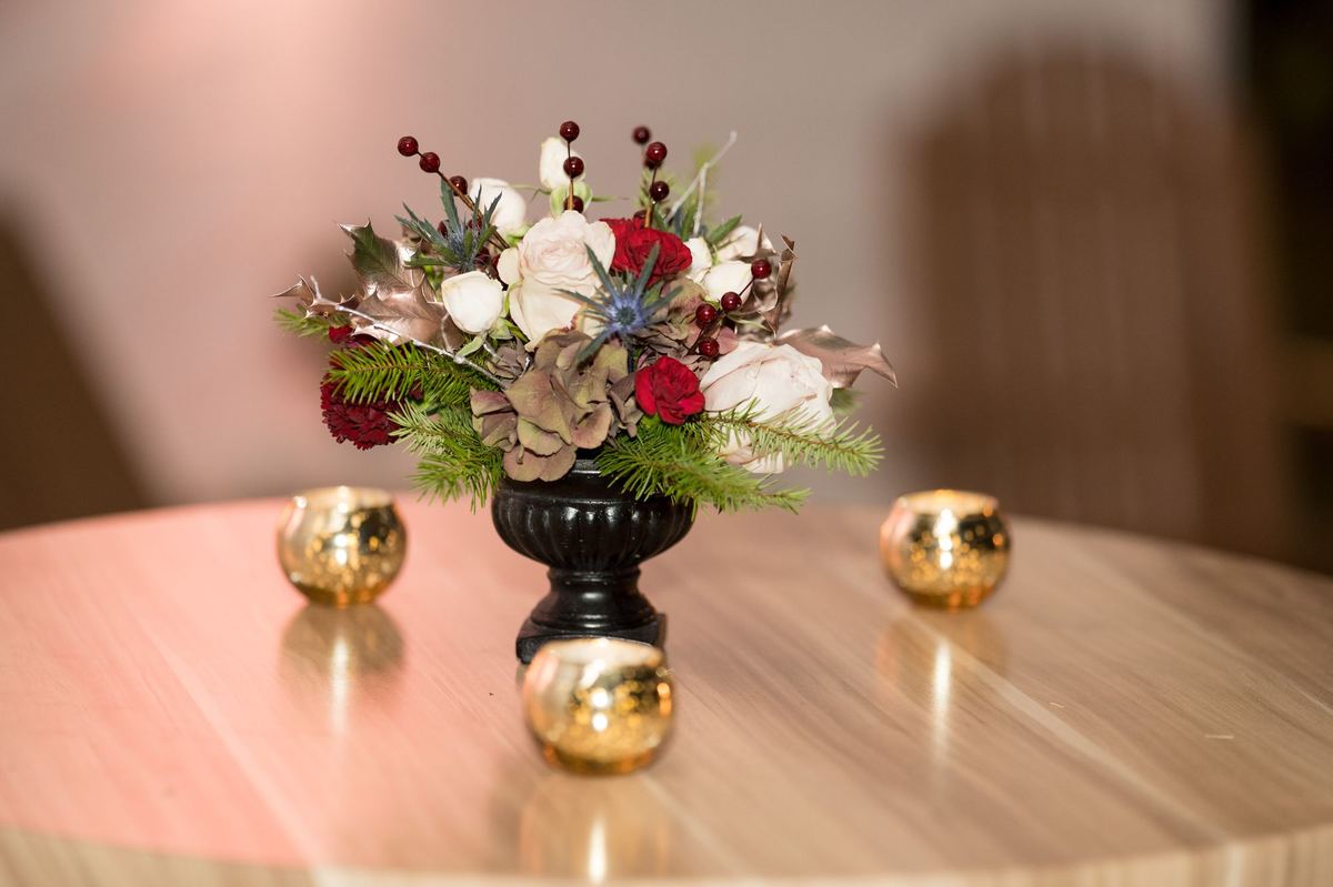 Holiday centerpiece of roses, berries and evergreen with gold candle holders